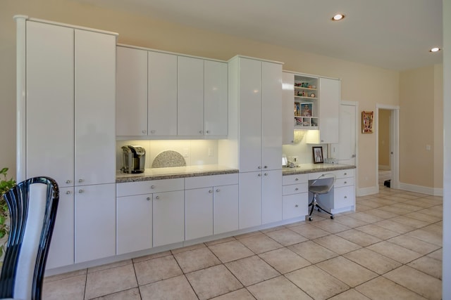 kitchen featuring built in desk, white cabinets, light tile patterned flooring, and light stone counters