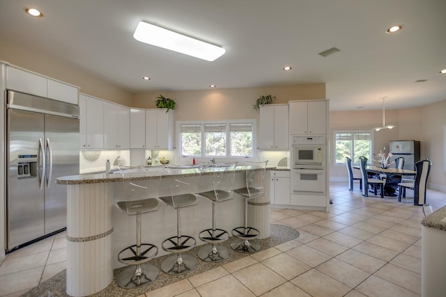 kitchen featuring white cabinets, stainless steel built in refrigerator, a center island with sink, and light tile patterned floors