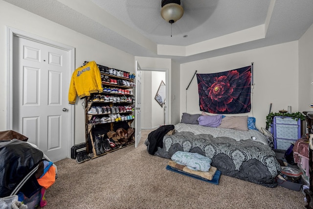 carpeted bedroom with a raised ceiling, ceiling fan, and a textured ceiling