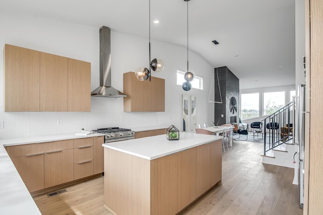 kitchen with light wood-type flooring, high end stainless steel range oven, a kitchen island, wall chimney exhaust hood, and lofted ceiling