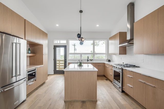 kitchen with wall chimney exhaust hood, light hardwood / wood-style flooring, a center island, premium appliances, and backsplash