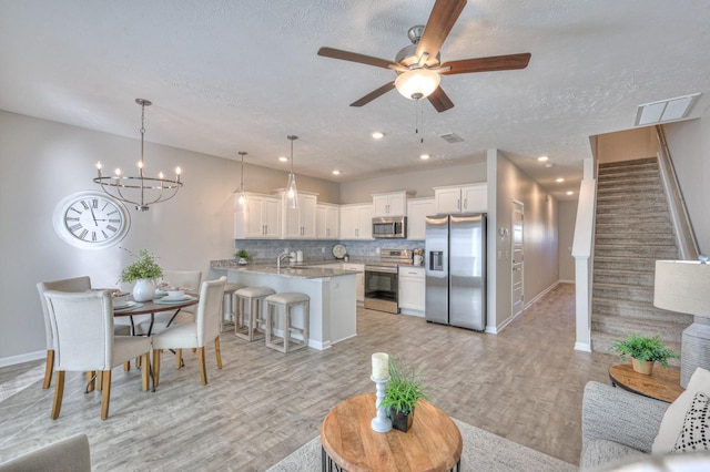 living room featuring ceiling fan with notable chandelier, light wood-type flooring, and a textured ceiling