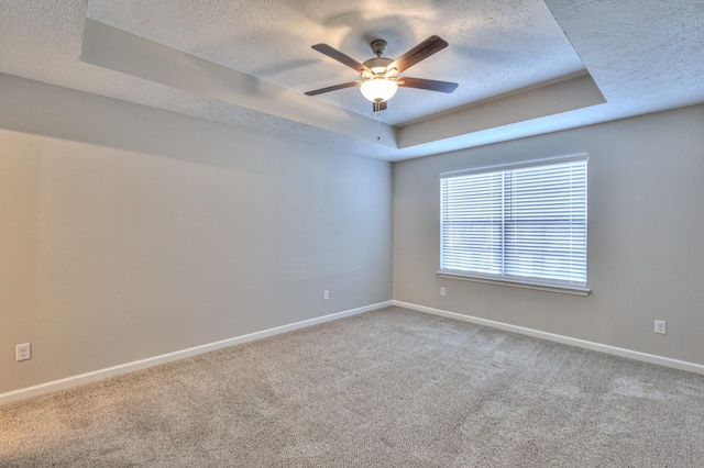 carpeted spare room with a textured ceiling, ceiling fan, and a raised ceiling