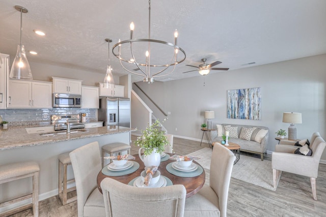 dining space with ceiling fan with notable chandelier, light wood-type flooring, a textured ceiling, and sink