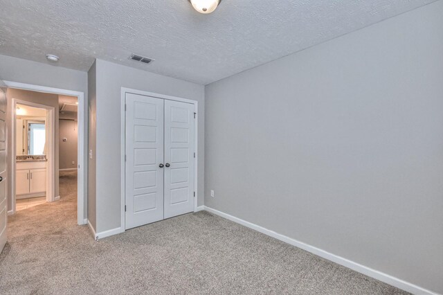 unfurnished bedroom featuring a textured ceiling, a closet, and light carpet