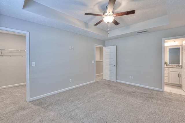 unfurnished bedroom featuring a closet, light carpet, ceiling fan, a spacious closet, and a tray ceiling