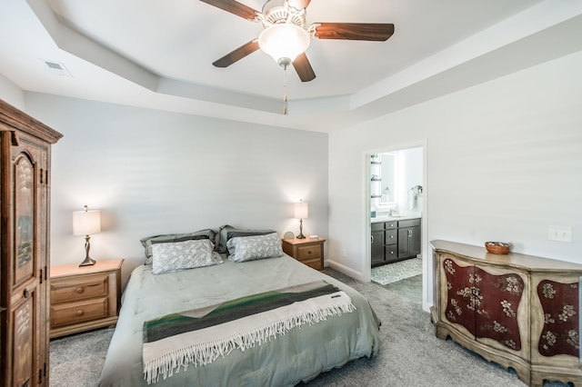 bedroom featuring ceiling fan, connected bathroom, carpet floors, and a tray ceiling