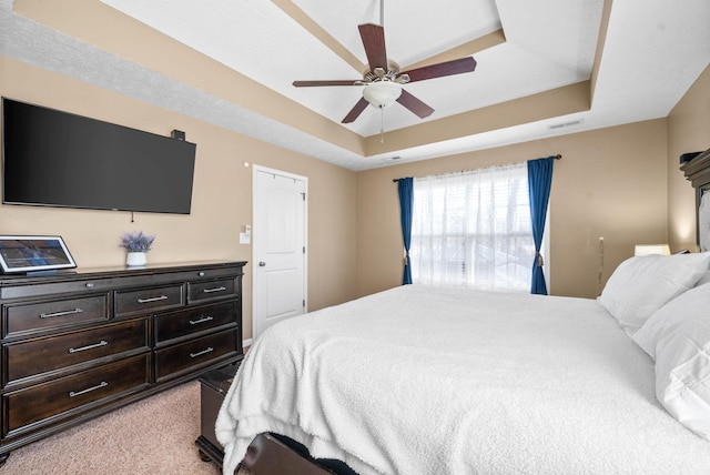 carpeted bedroom with a raised ceiling and ceiling fan