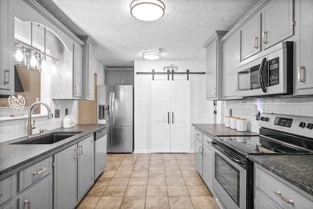 kitchen featuring a barn door, backsplash, gray cabinetry, appliances with stainless steel finishes, and sink