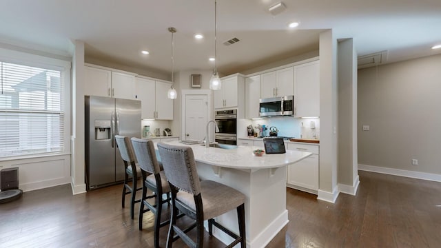 kitchen featuring a kitchen island with sink, appliances with stainless steel finishes, white cabinetry, and pendant lighting