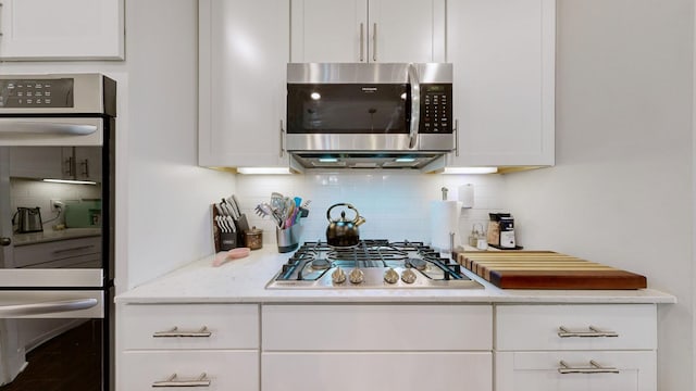 kitchen featuring stainless steel appliances, white cabinets, tasteful backsplash, and light stone countertops