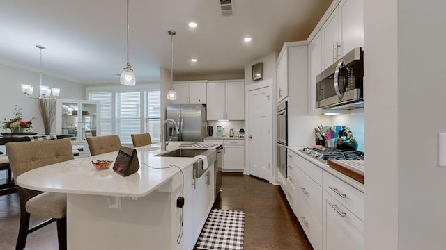 kitchen featuring appliances with stainless steel finishes, white cabinets, hanging light fixtures, and an island with sink