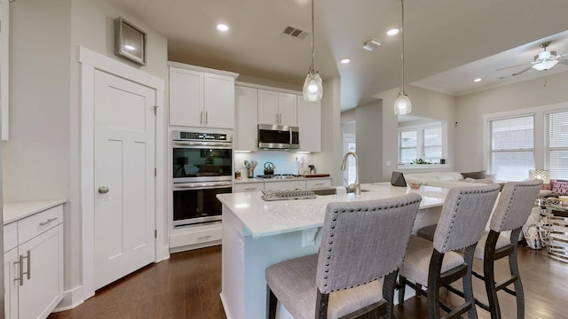 kitchen featuring appliances with stainless steel finishes, decorative light fixtures, white cabinetry, a kitchen island with sink, and ceiling fan