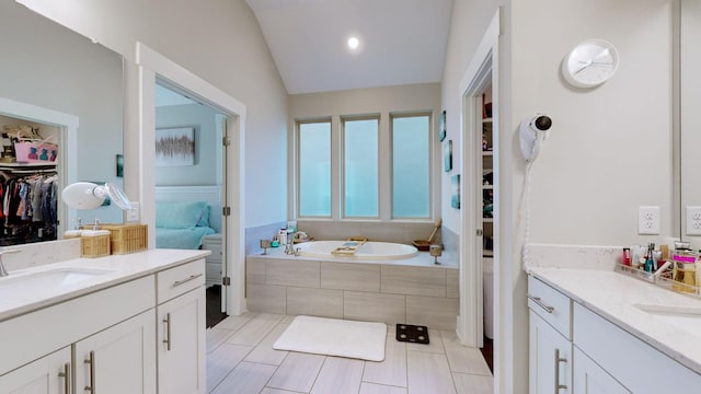 bathroom featuring a relaxing tiled tub, vanity, lofted ceiling, and tile patterned flooring