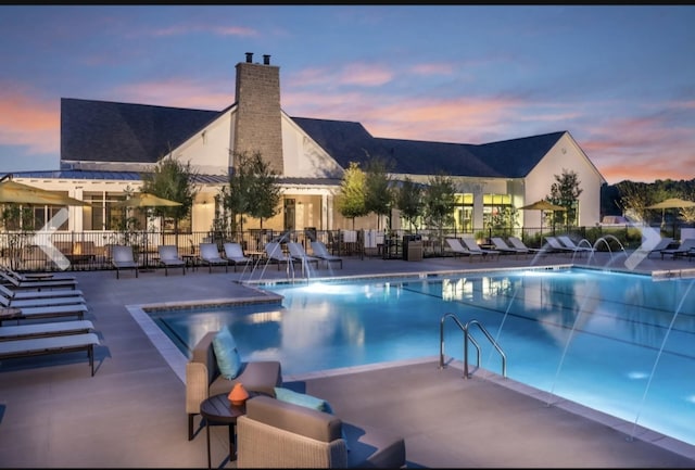 pool at dusk with pool water feature and a patio