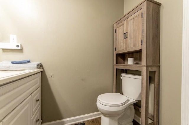 half bath featuring baseboards, vanity, toilet, and wood finished floors