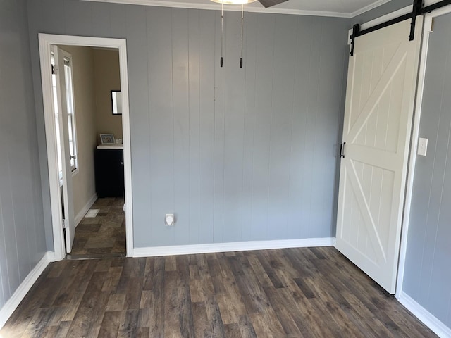 unfurnished bedroom featuring baseboards, a barn door, dark wood-type flooring, and crown molding