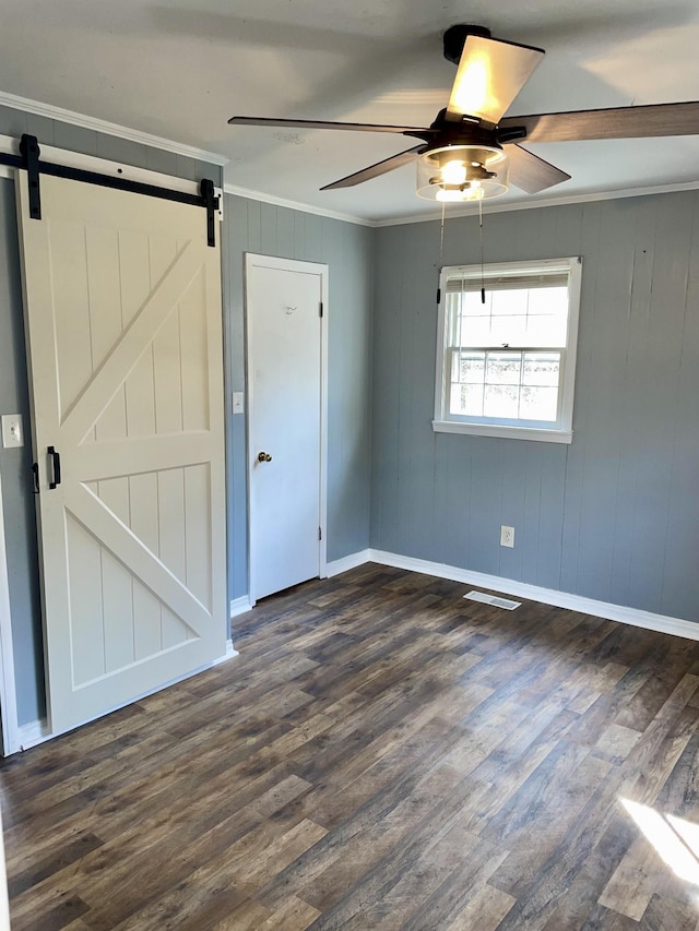 unfurnished room with a barn door, dark wood finished floors, visible vents, and crown molding