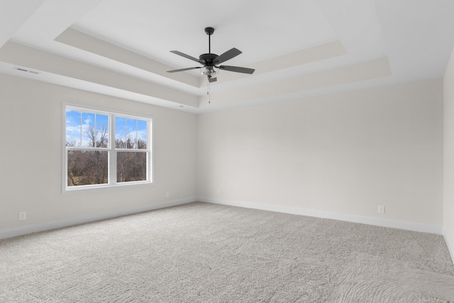 carpeted spare room featuring a raised ceiling and ceiling fan