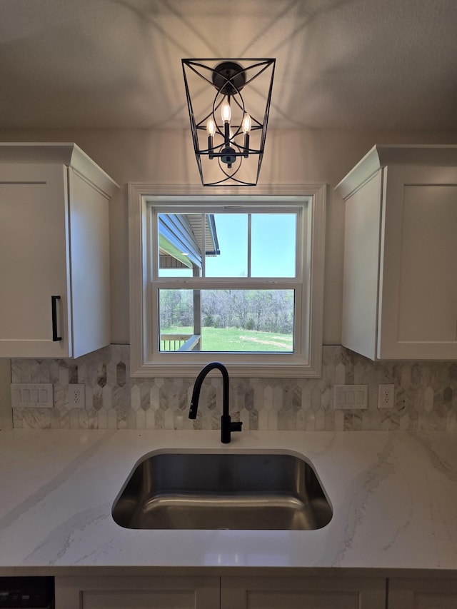 kitchen with white cabinets, tasteful backsplash, a notable chandelier, and a sink