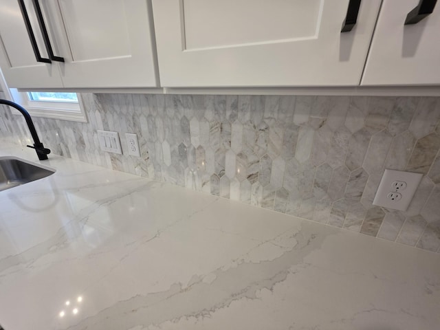 room details with light stone counters, a sink, and white cabinetry