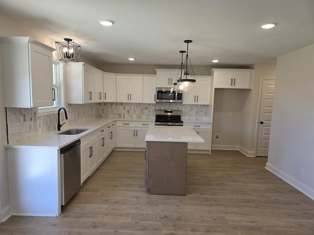 kitchen featuring white cabinets, appliances with stainless steel finishes, light countertops, a sink, and backsplash
