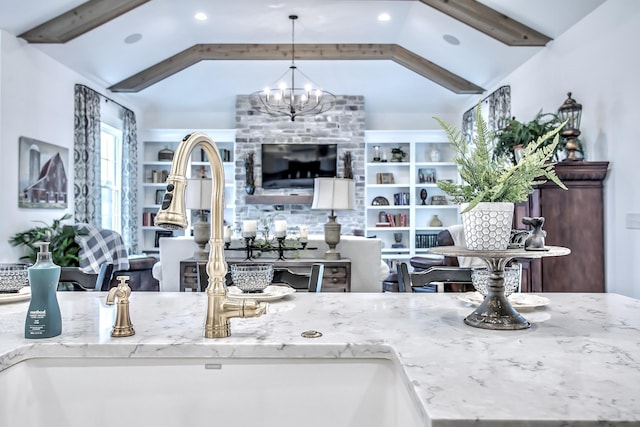 kitchen featuring light stone counters, vaulted ceiling, a chandelier, pendant lighting, and sink