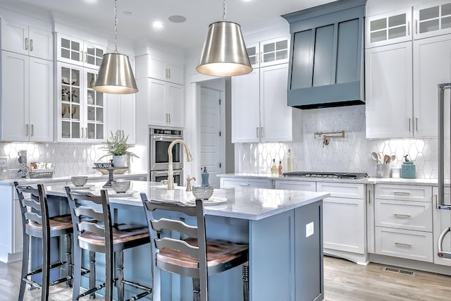 kitchen with white cabinets, decorative light fixtures, a kitchen island with sink, and a breakfast bar area