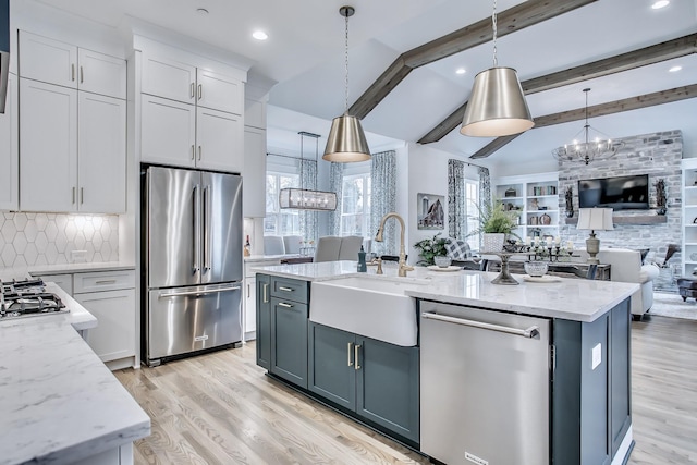 kitchen featuring decorative light fixtures, light stone counters, tasteful backsplash, a kitchen island with sink, and appliances with stainless steel finishes