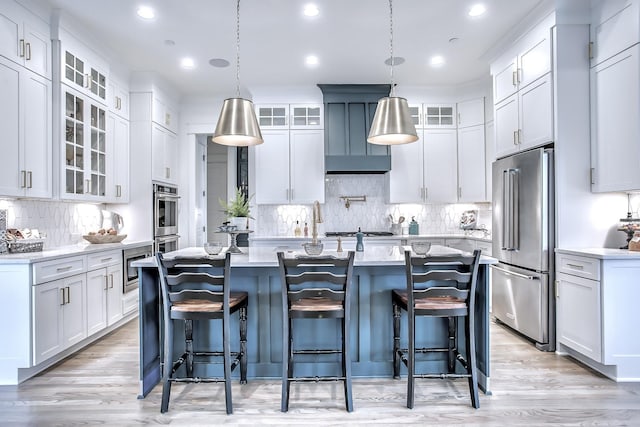 kitchen with decorative light fixtures, stainless steel appliances, a center island with sink, a breakfast bar, and white cabinetry