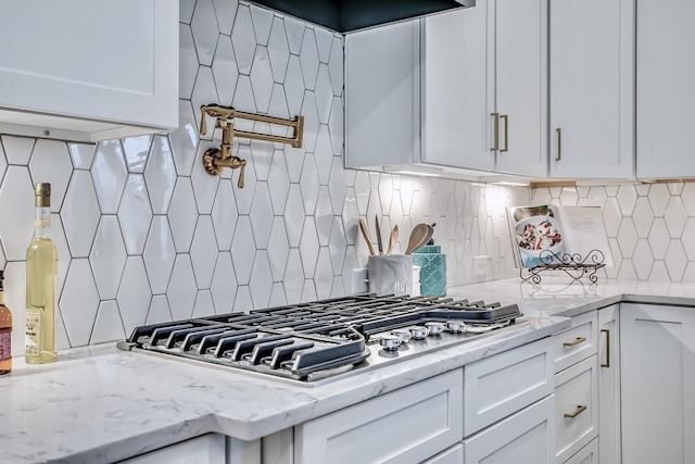 kitchen featuring light stone counters, white cabinets, and backsplash