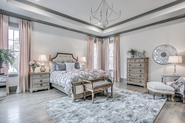 bedroom featuring a raised ceiling, light wood-type flooring, multiple windows, and ornamental molding