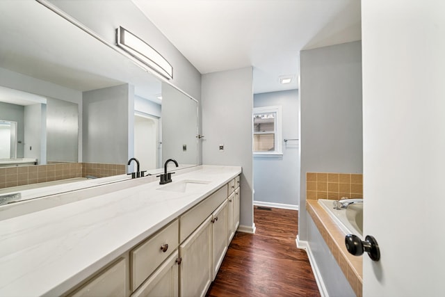 bathroom with wood-type flooring, vanity, and tiled bath