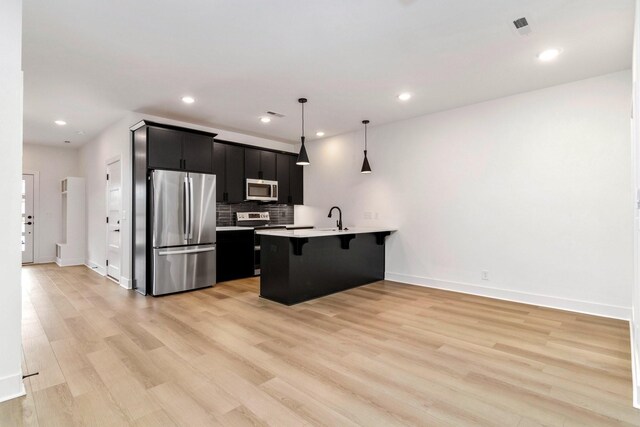 kitchen with a breakfast bar area, hanging light fixtures, stainless steel appliances, decorative backsplash, and light wood-type flooring