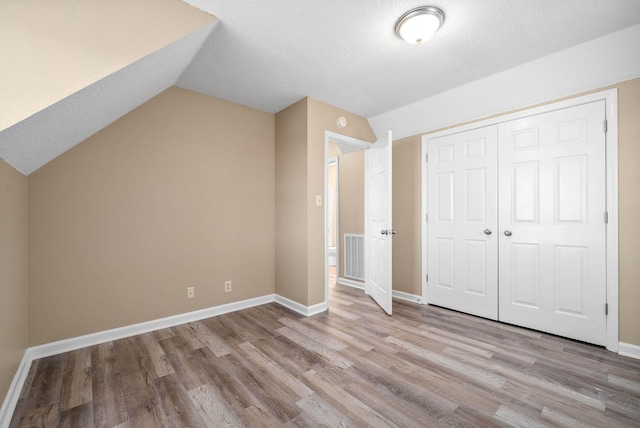 unfurnished bedroom with lofted ceiling, light wood-type flooring, a textured ceiling, and a closet