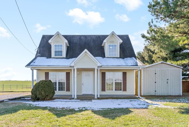 cape cod home with a front lawn and a storage shed