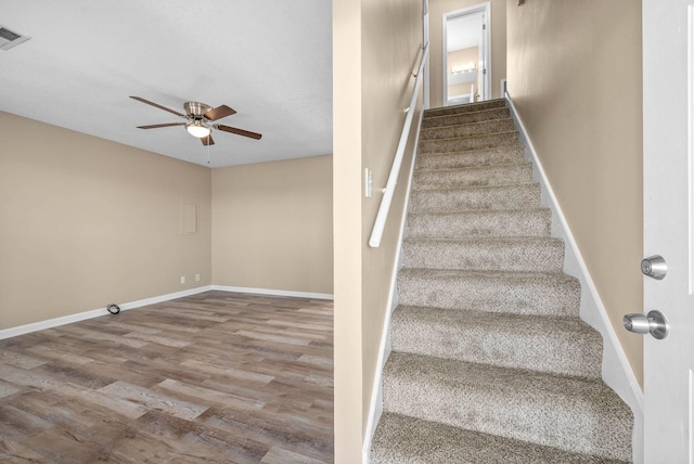 stairs featuring ceiling fan and hardwood / wood-style floors