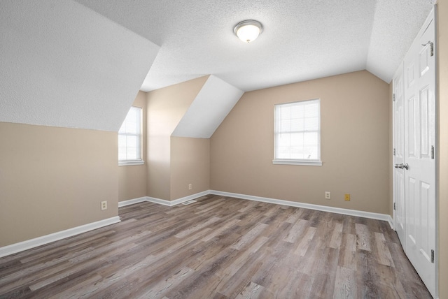 bonus room with lofted ceiling, light wood-type flooring, and a textured ceiling