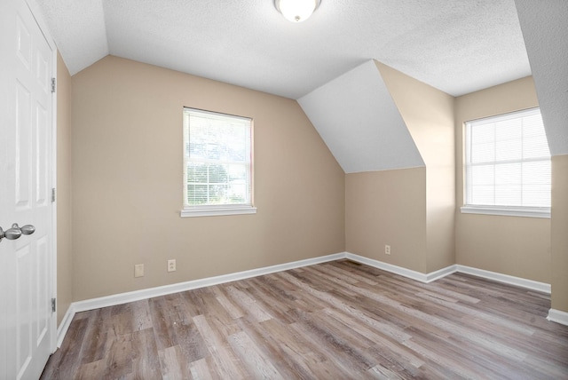 bonus room featuring a textured ceiling, light wood-type flooring, lofted ceiling, and plenty of natural light