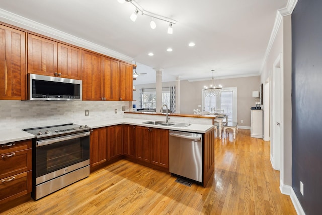 kitchen with kitchen peninsula, stainless steel appliances, ceiling fan with notable chandelier, ornamental molding, and sink