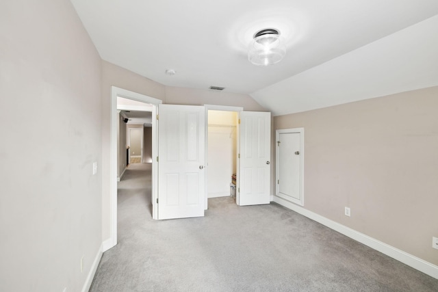 unfurnished bedroom with vaulted ceiling, a walk in closet, a closet, and light carpet