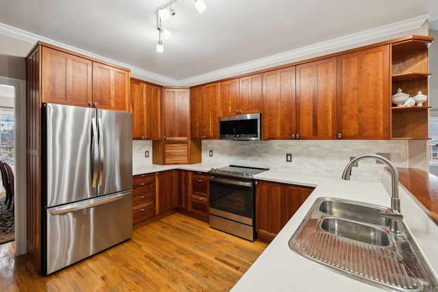 kitchen with sink, light wood-type flooring, tasteful backsplash, crown molding, and appliances with stainless steel finishes