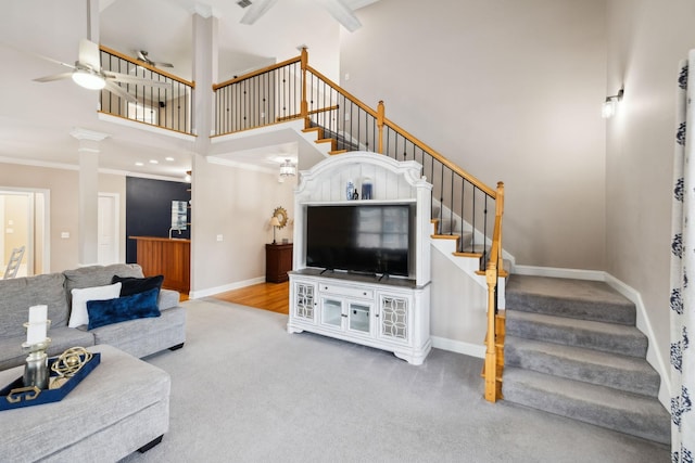 living room featuring carpet, a towering ceiling, crown molding, ceiling fan, and decorative columns