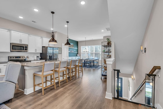 kitchen featuring appliances with stainless steel finishes, hanging light fixtures, an island with sink, a kitchen bar, and white cabinets