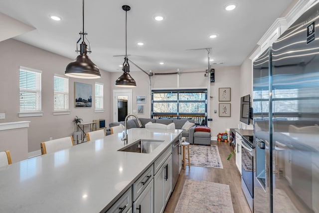 kitchen featuring appliances with stainless steel finishes, pendant lighting, a kitchen bar, sink, and light hardwood / wood-style flooring