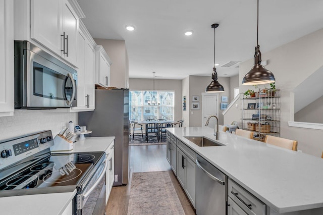 kitchen featuring a kitchen island with sink, stainless steel appliances, sink, white cabinetry, and decorative light fixtures