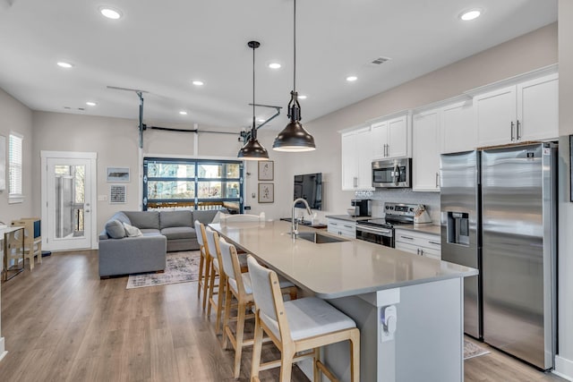 kitchen with a kitchen island with sink, appliances with stainless steel finishes, pendant lighting, white cabinets, and sink