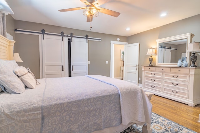 bedroom with ceiling fan, light hardwood / wood-style floors, and a barn door