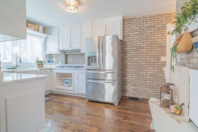 kitchen with stainless steel appliances, backsplash, brick wall, dark hardwood / wood-style flooring, and white cabinets