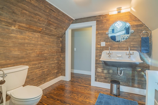 bathroom featuring toilet, lofted ceiling, wooden walls, and sink